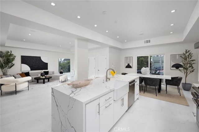 kitchen featuring a center island with sink, white cabinets, dishwasher, open floor plan, and a tray ceiling