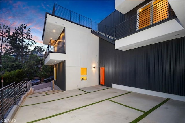 back of house at dusk featuring a patio area, a balcony, and stucco siding