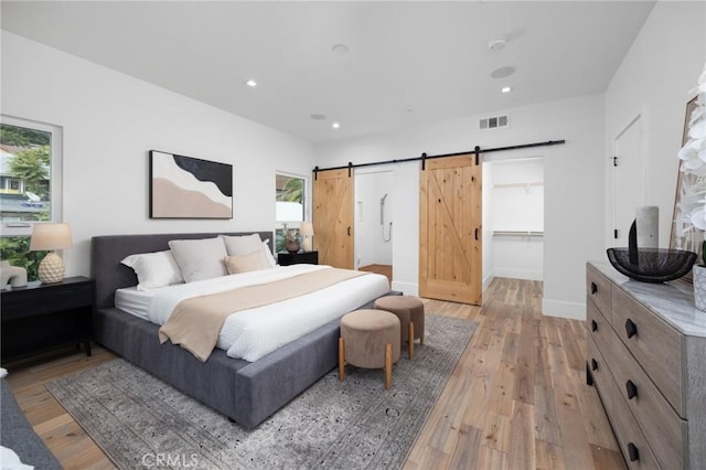 bedroom featuring a barn door, recessed lighting, visible vents, baseboards, and light wood-type flooring