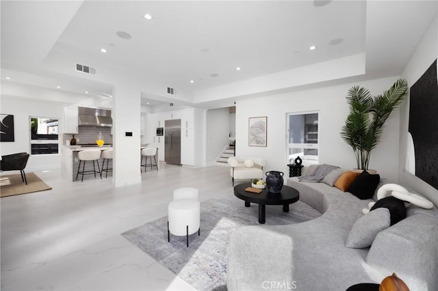 living area with a tray ceiling, visible vents, stairway, and recessed lighting