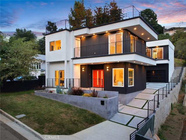 modern home featuring a balcony, driveway, a lawn, and stucco siding