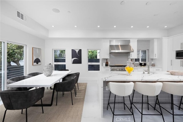 kitchen featuring a sink, visible vents, white cabinetry, decorative backsplash, and wall chimney exhaust hood