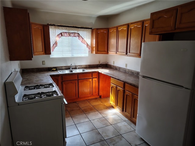 kitchen with light tile patterned flooring, white appliances, a sink, brown cabinetry, and dark countertops