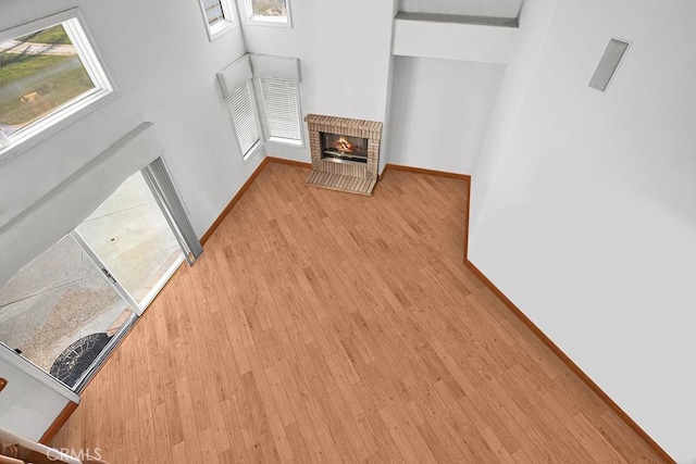 unfurnished living room featuring light wood-type flooring, a brick fireplace, and baseboards