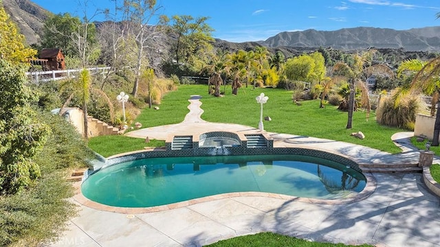 view of swimming pool featuring a pool with connected hot tub, a mountain view, and a yard