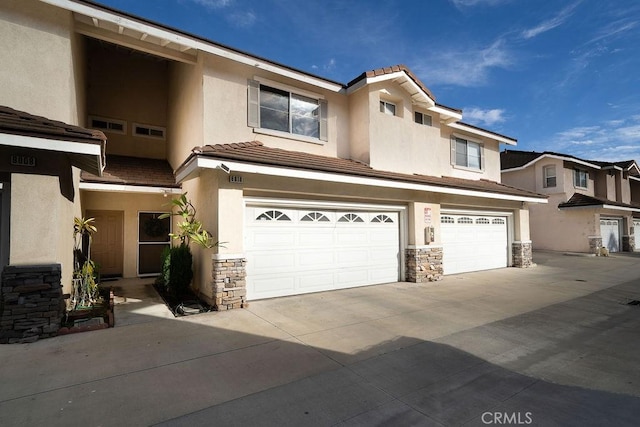 view of property featuring stone siding, concrete driveway, an attached garage, and stucco siding