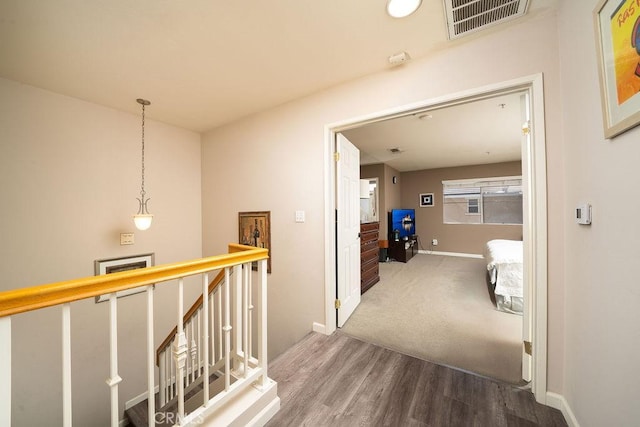 corridor featuring baseboards, visible vents, wood finished floors, and an upstairs landing