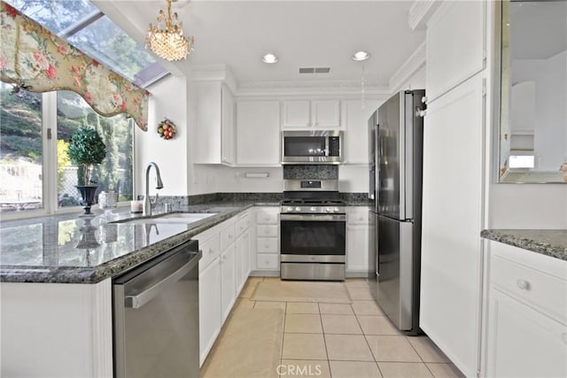 kitchen featuring light tile patterned floors, stainless steel appliances, a sink, white cabinetry, and dark stone countertops