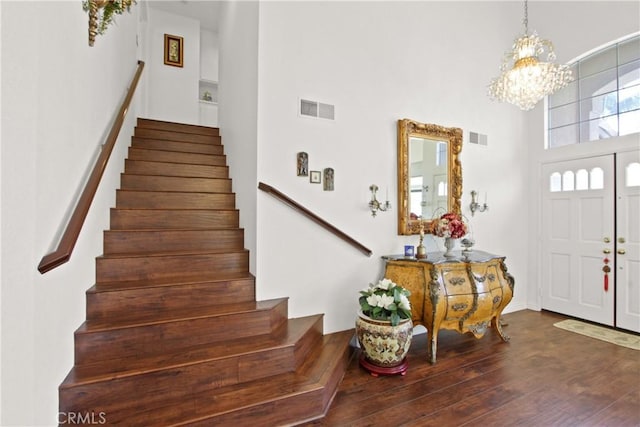 entrance foyer with visible vents, stairway, an inviting chandelier, and wood finished floors