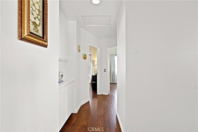 hall featuring dark wood-style floors, attic access, and baseboards