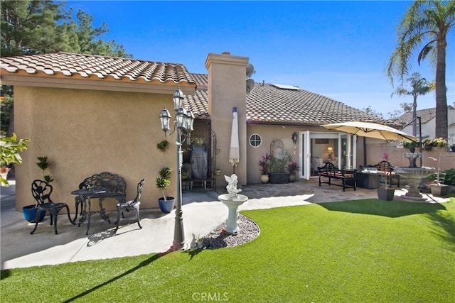 rear view of property with a yard, a patio, a chimney, stucco siding, and a tiled roof