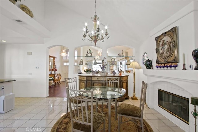 dining area with light tile patterned floors, a notable chandelier, arched walkways, and a tiled fireplace