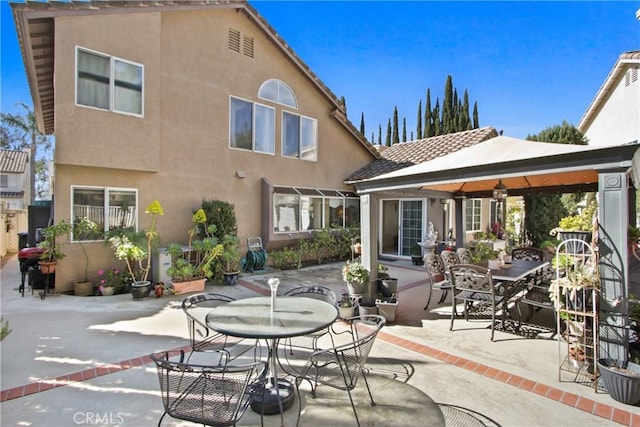 rear view of house featuring a patio, outdoor dining space, a gazebo, and stucco siding