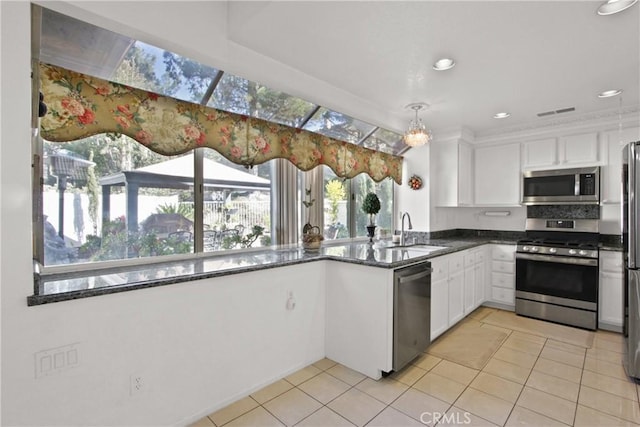 kitchen featuring stainless steel appliances, dark stone counters, white cabinets, and a sink