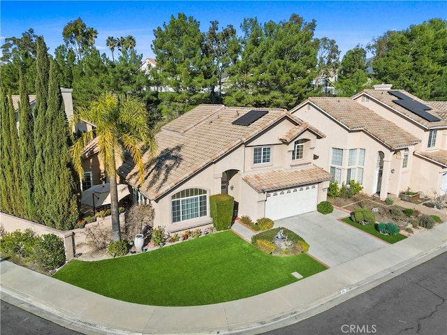 view of front facade with concrete driveway, a tile roof, an attached garage, roof mounted solar panels, and a front lawn