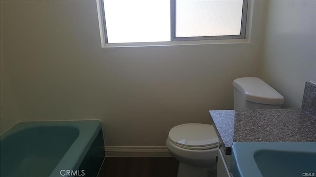 bathroom with a tub, baseboards, vanity, and toilet