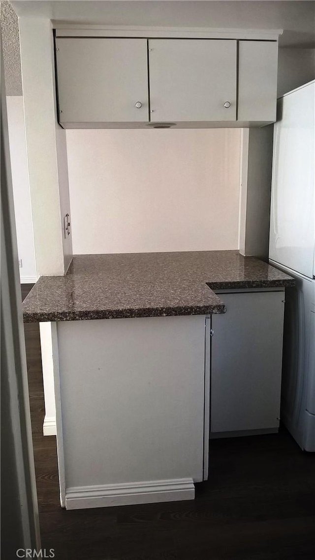 kitchen featuring dark stone counters, a peninsula, freestanding refrigerator, and white cabinets