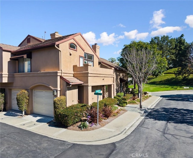 view of front facade with driveway, a chimney, an attached garage, and stucco siding