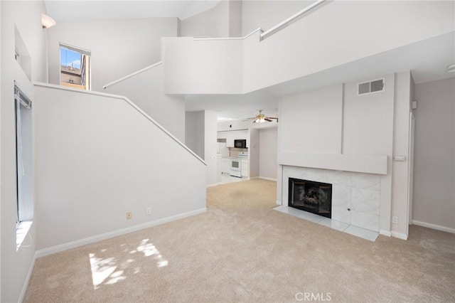 unfurnished living room featuring a towering ceiling, carpet, visible vents, and a tile fireplace