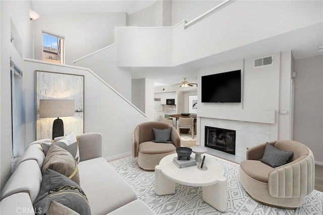 living room with a high ceiling, a tiled fireplace, visible vents, and baseboards