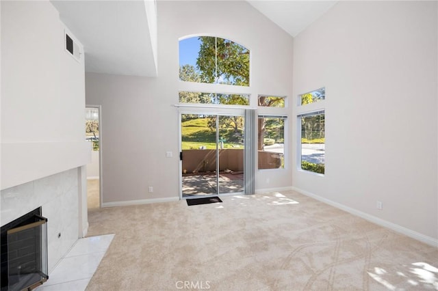 unfurnished living room featuring baseboards, visible vents, a tile fireplace, carpet floors, and high vaulted ceiling