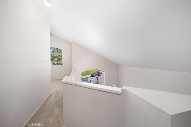 hall with light carpet, vaulted ceiling, an upstairs landing, and baseboards