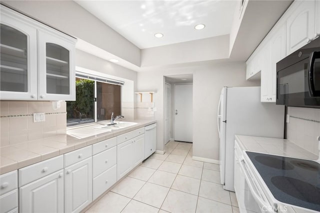 kitchen with tile countertops, white appliances, white cabinetry, backsplash, and glass insert cabinets