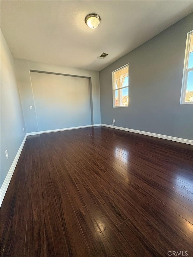 spare room featuring dark wood-type flooring, visible vents, and baseboards