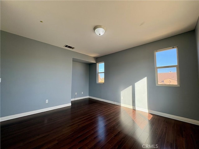 spare room featuring dark wood-style floors, visible vents, and baseboards