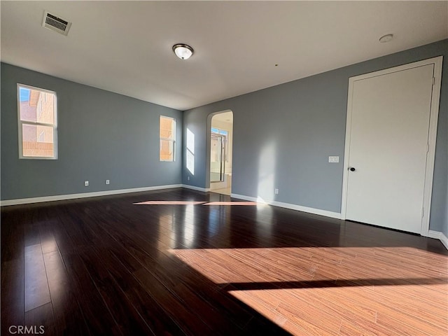 spare room with wood-type flooring, visible vents, arched walkways, and baseboards