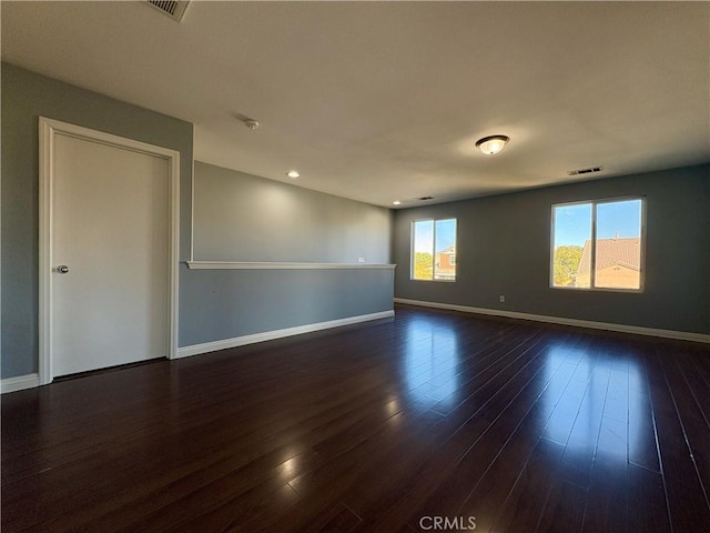 empty room with visible vents, dark wood finished floors, and baseboards