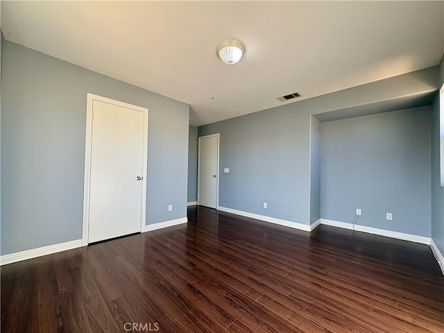 unfurnished room with visible vents, baseboards, and dark wood-style flooring