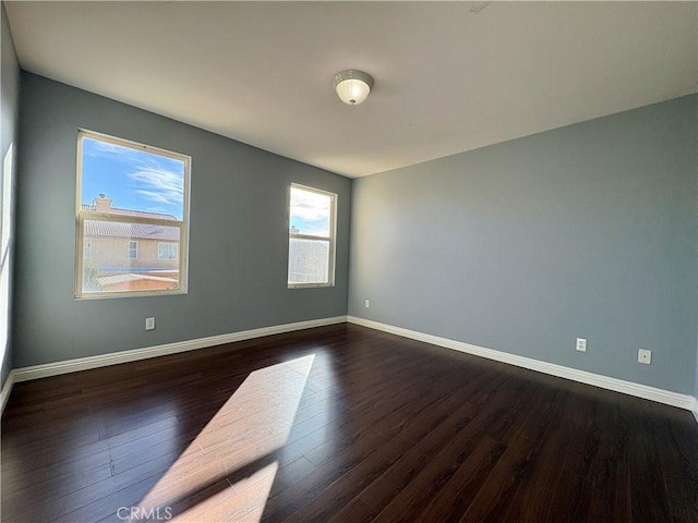 spare room featuring dark wood-type flooring and baseboards