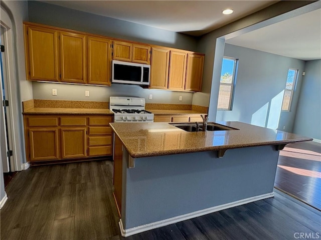 kitchen with white appliances, a sink, a kitchen breakfast bar, light stone countertops, and dark wood finished floors