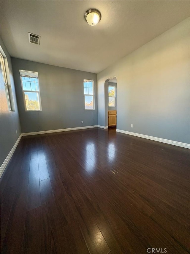 spare room featuring baseboards, visible vents, arched walkways, and dark wood-type flooring