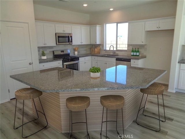 kitchen with light wood finished floors, stainless steel appliances, tasteful backsplash, white cabinets, and a sink