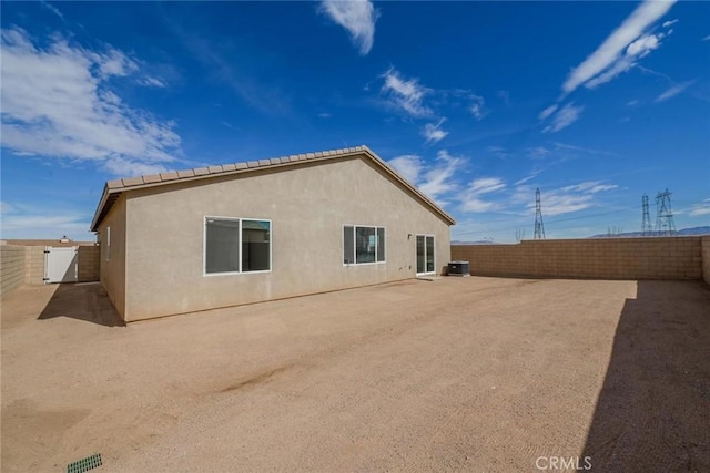 back of house featuring a gate, central AC, a fenced backyard, and stucco siding