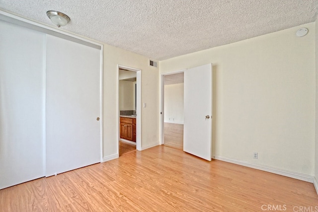 unfurnished bedroom with a textured ceiling, visible vents, baseboards, a closet, and light wood finished floors