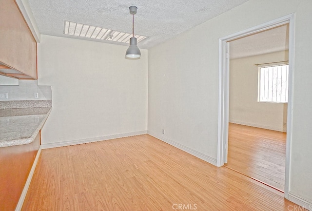 unfurnished dining area with a textured ceiling, light wood-type flooring, and baseboards