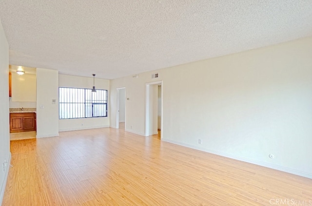 unfurnished room with light wood finished floors, baseboards, visible vents, and a textured ceiling