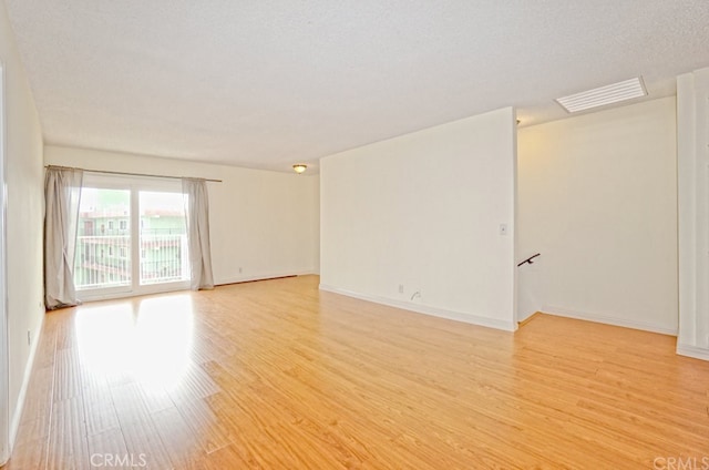 empty room featuring light wood-style floors, visible vents, a textured ceiling, and baseboards