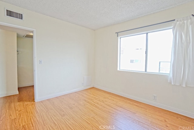 empty room with light wood-type flooring, visible vents, a textured ceiling, and baseboards