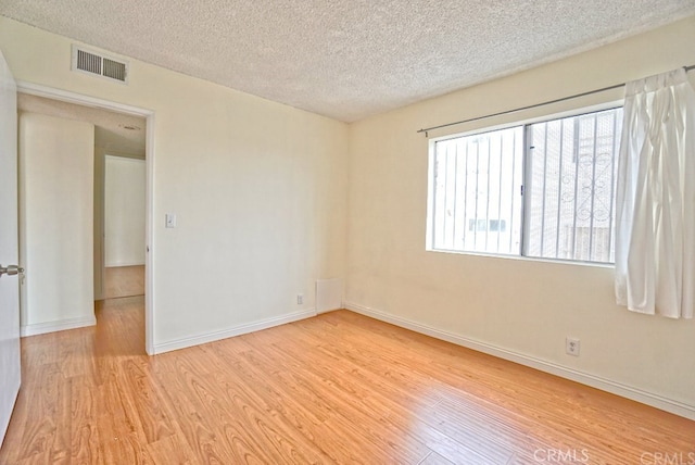 spare room with light wood-style floors, baseboards, visible vents, and a textured ceiling