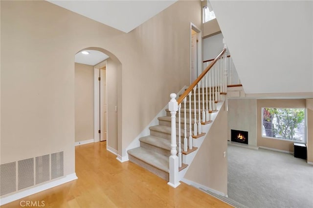 staircase with arched walkways, wood finished floors, visible vents, and baseboards