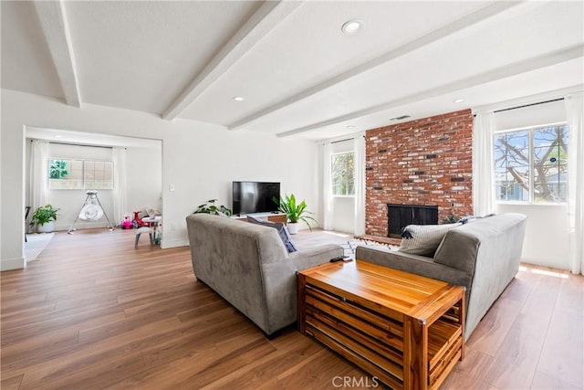 living area with a healthy amount of sunlight, light wood finished floors, a brick fireplace, and beam ceiling