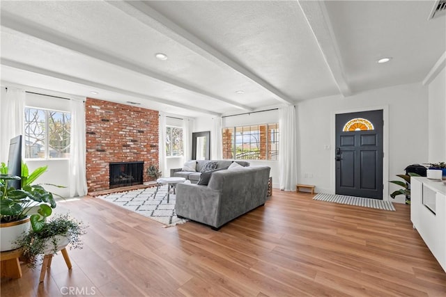 living room with visible vents, a brick fireplace, a textured ceiling, light wood-type flooring, and beamed ceiling