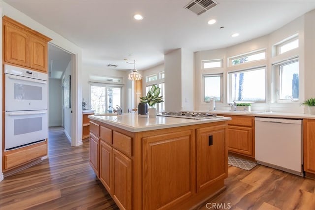 kitchen featuring a kitchen island with sink, white appliances, wood finished floors, and visible vents