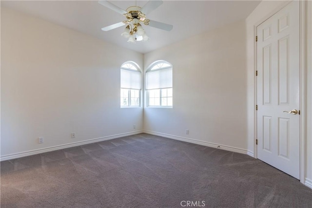 spare room with dark carpet, baseboards, and ceiling fan