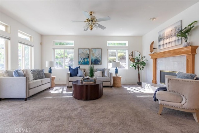 carpeted living room featuring a ceiling fan, a tile fireplace, and baseboards