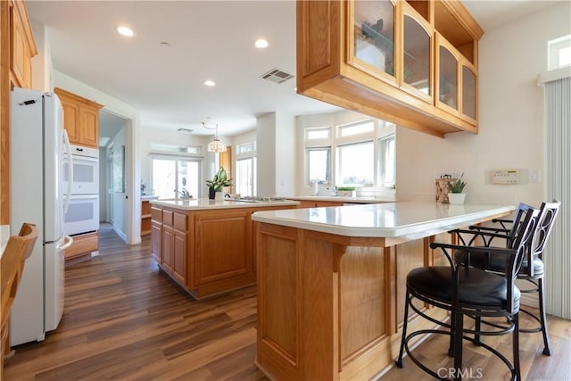 kitchen featuring dark wood-style flooring, visible vents, glass insert cabinets, white appliances, and a peninsula